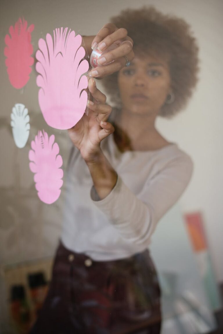 concentrated black female artisan sticking paper flowers on glass wall