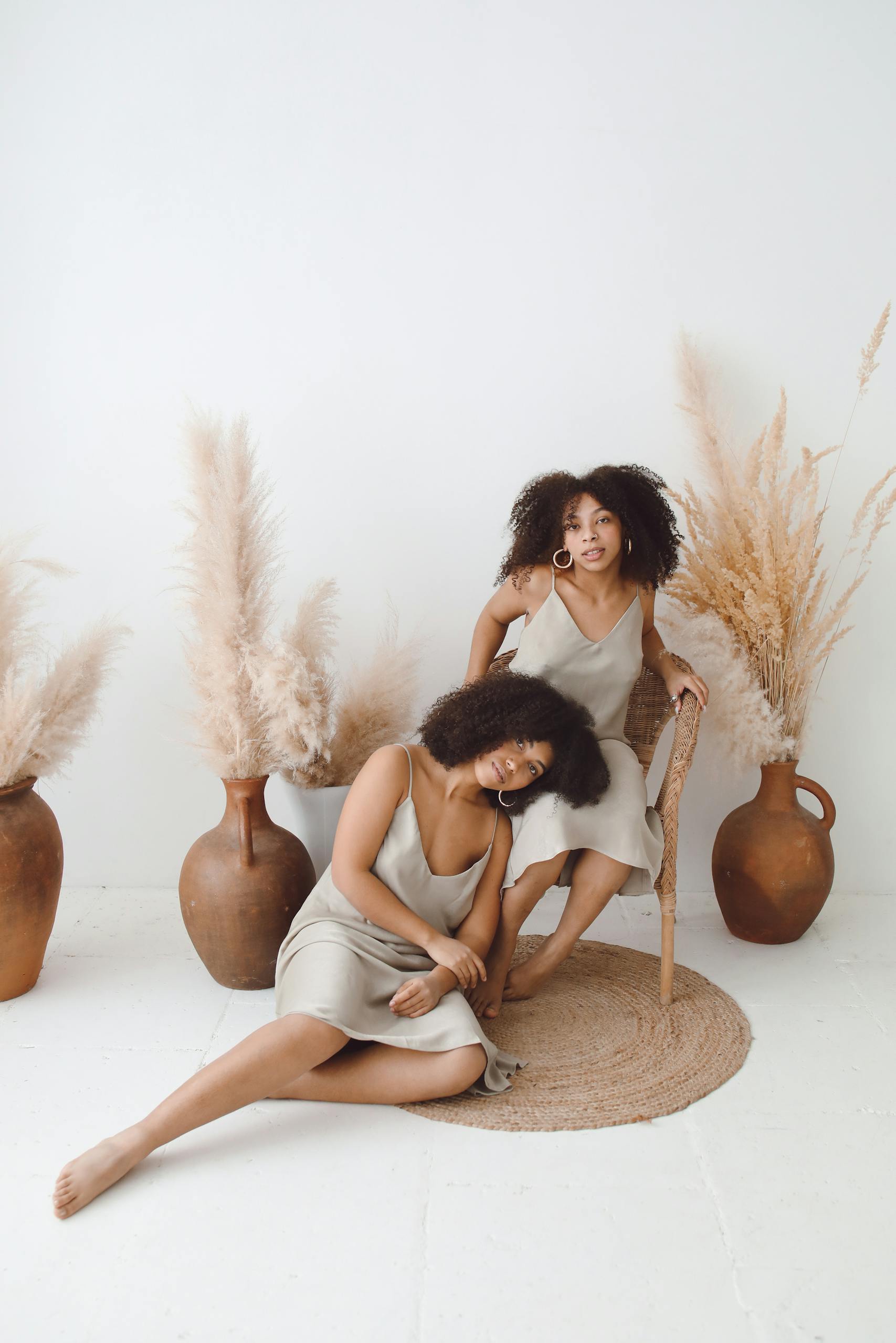 Charming portrait of two women in silk dresses surrounded by pampas grass in a minimalist setting.