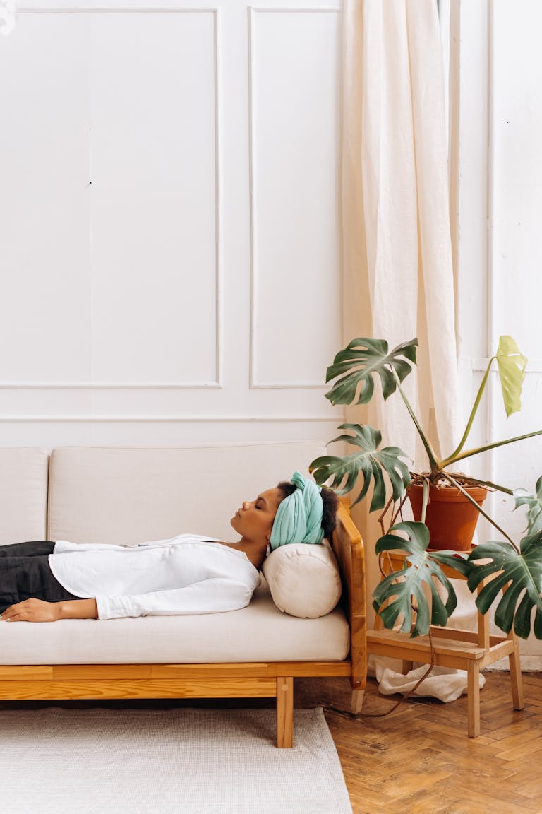 Adult woman relaxing indoors with a monstera plant beside her on a comfortable beige sofa.