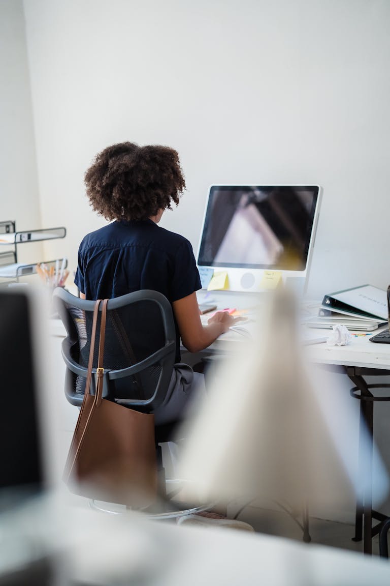 A woman with curly hair concentrates on computer work at an office desk.