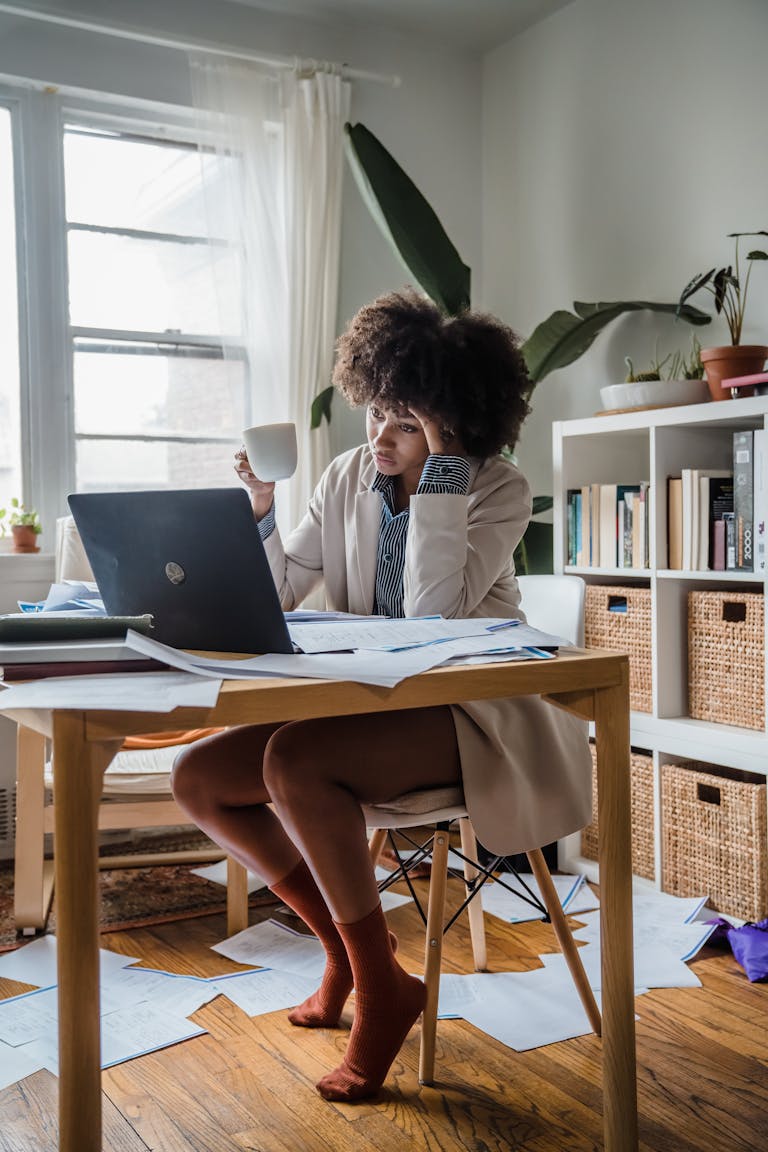 Woman experiences burnout while working remotely, surrounded by papers and a laptop. Survival mode. Mrs Mummy PhD.